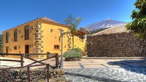A yellow building with stone accents, a stone wall, and a mountain in the background. - Finca Casonas de Marengo (Icod de los Vinos)