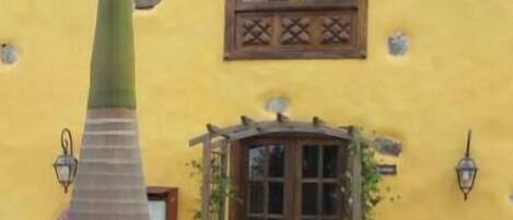 Un edificio amarillo con una ventana, una puerta y un pequeño jardín lleno de flores rosas.
