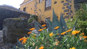 A yellow building with stone accents, large windows, and a garden with orange flowers. - Finca Casonas de Marengo (Icod de los Vinos)