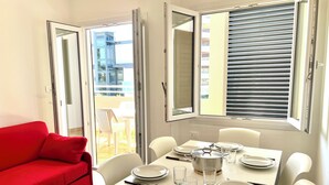 En matplats med ett bord dukat för fyra personer, en röd soffa och en balkong med utsikt över byggnaderna.