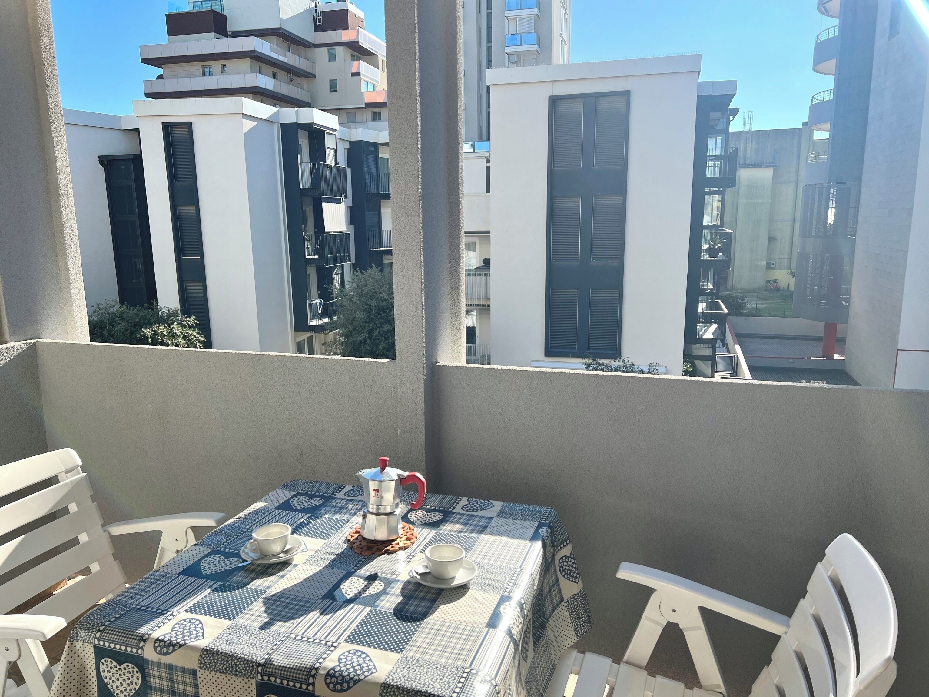 A balcony with a table set for two, a coffee pot, and white chairs.
