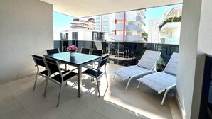 A balcony with a table and chairs, a sun lounger, and a view of buildings. - Lignano Sabbiadoro central flat (Lignano Sabbiadoro)