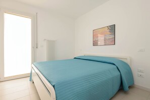 Um quarto com cama, radiador, porta e um quadro fixado na parede.