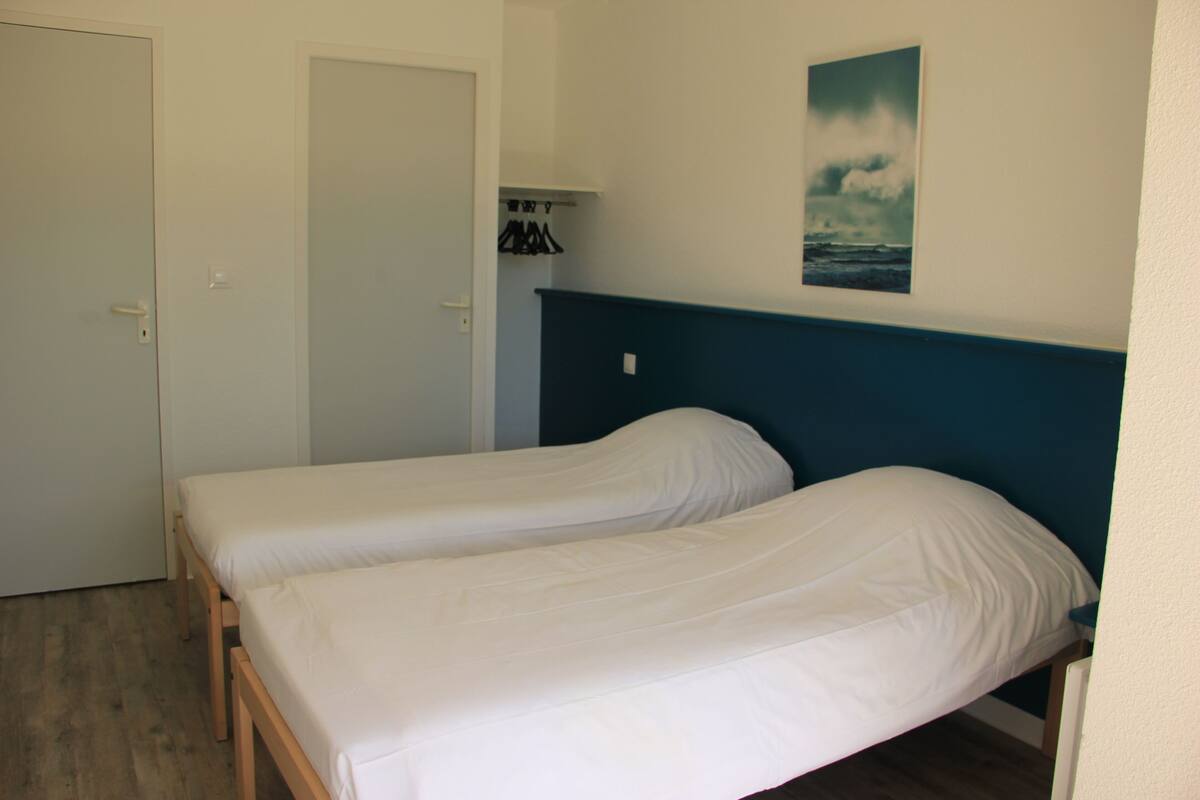 Une chambre avec deux lits simples, une porte, un porte-manteau et un tableau au mur.