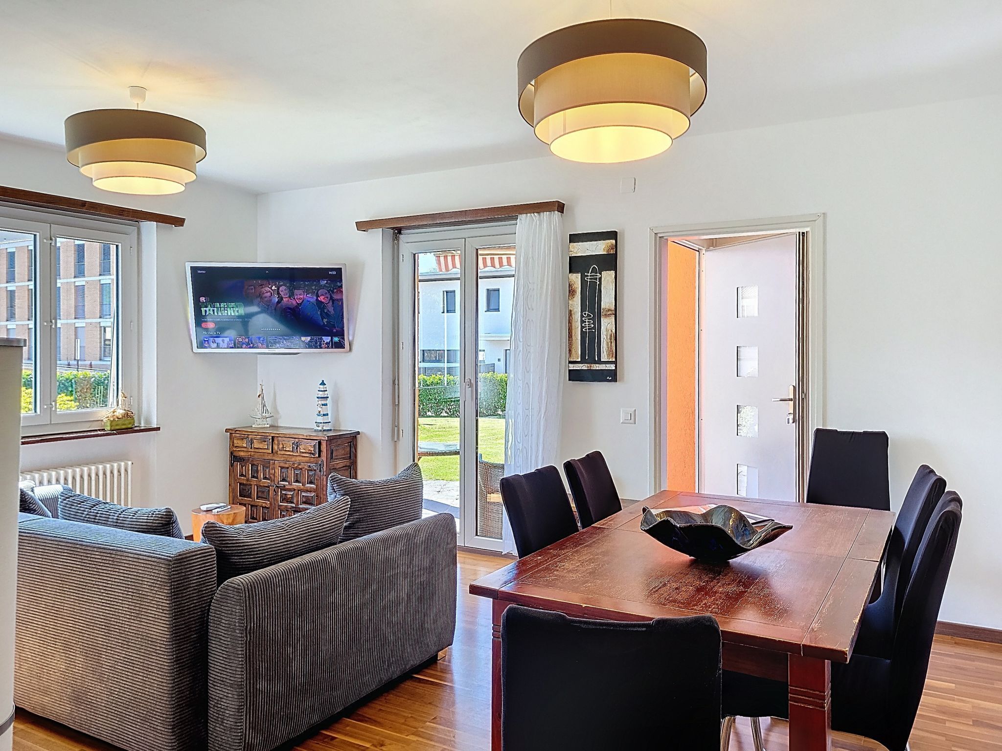 A modern living room with a sofa, dining table, chairs, a TV, and a view of the outdoors.