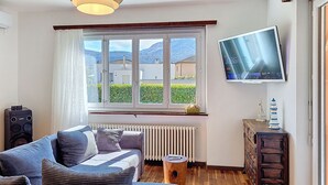 Ett vardagsrum med en soffa, en tv, ett element och ett fönster med utsikt över byggnader och kullar.