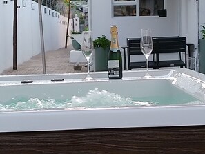 Boblebad med to glas og en champagneflaske, en sort stol og en hvid væg med et vindue.