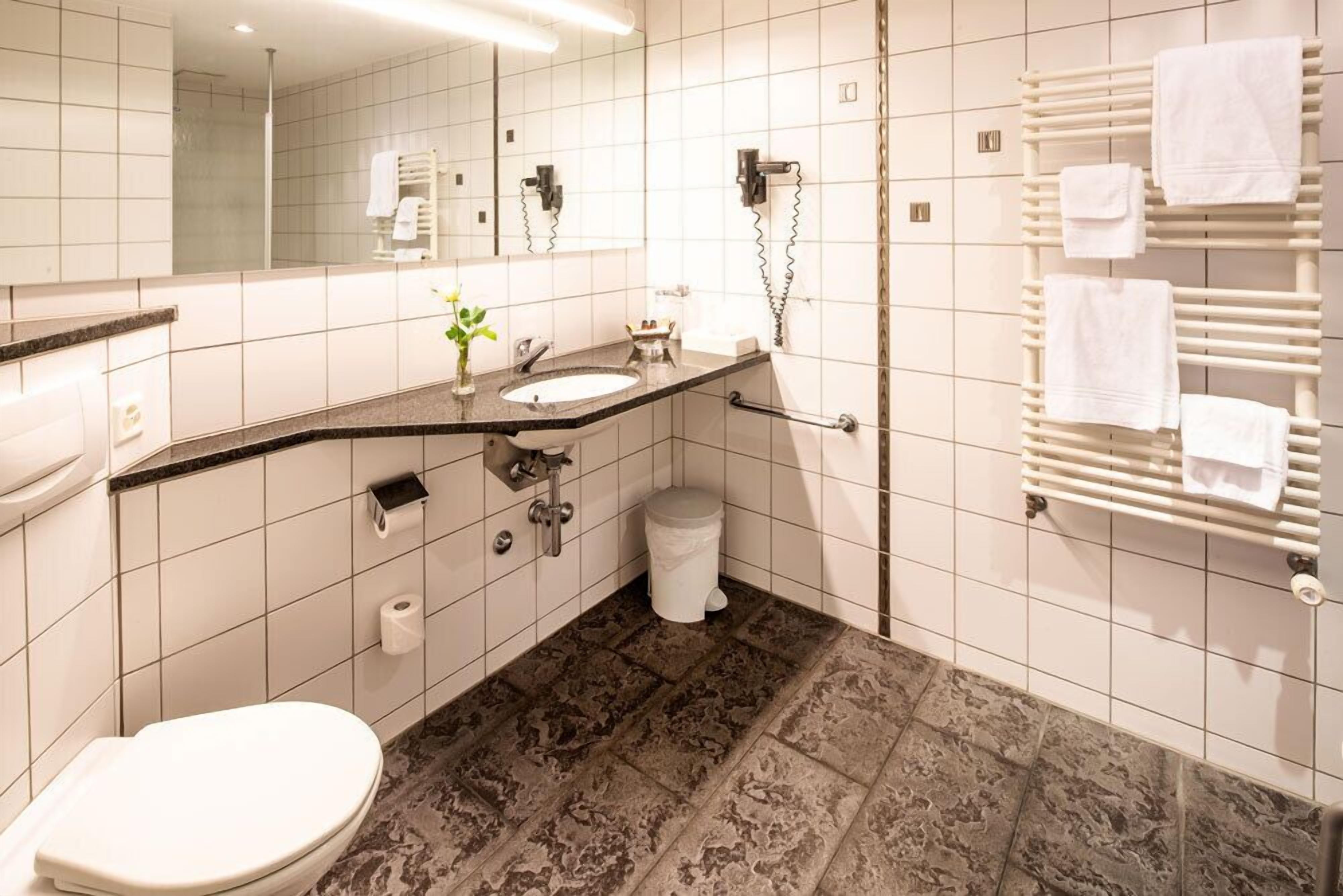 Un bagno moderno con un water bianco, un lavabo con specchio, un portasciugamani e una zona doccia.