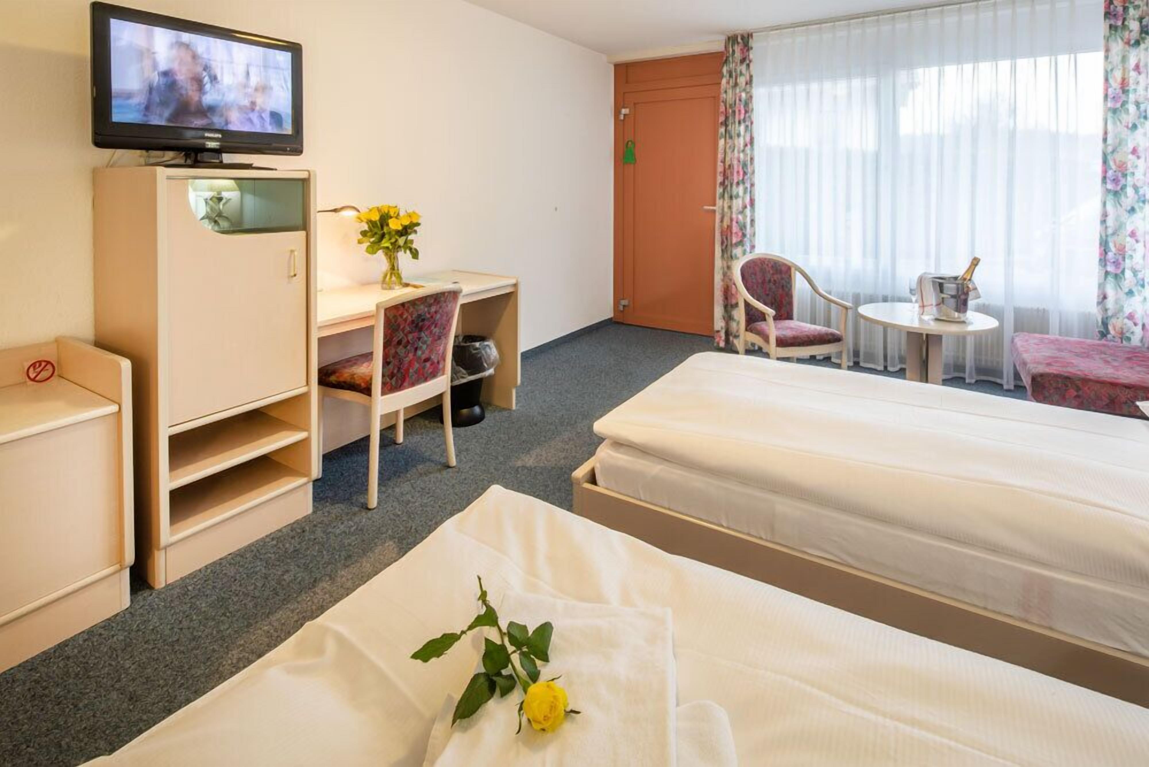 Habitación de hotel con dos camas, un escritorio con televisor, una mesita con una botella y una silla.