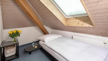 A bedroom with a sloped ceiling, a bed, a bedside table with a vase of flowers, and a radiator.
