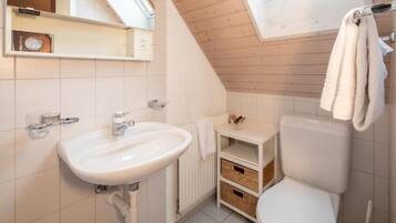 Ein kleines, modernes Badezimmer mit einem weißen Waschbecken, einer Toilette und einer Holzboden.