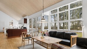 Ein geräumiger Wohnbereich mit Holzboden, einem zentralen Tisch, einer Couch und einer Küche im Hintergrund.