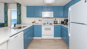 A modern kitchen with blue cabinets, white appliances, and a view to the left. - Cozy 2-bedroom condo on the 10th Floor, located in fantastic North Myrtle Beach (North Myrtle Beach)