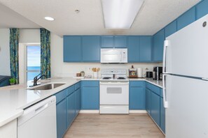 A modern kitchen with blue cabinets, white appliances, and a view to the left. - Cozy 2-bedroom condo on the 10th Floor, located in fantastic North Myrtle Beach (North Myrtle Beach)