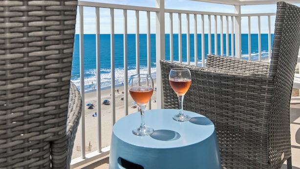 A balcony with wicker furniture, two glasses of a pink beverage, and a view of the ocean. - Cozy 2-bedroom condo on the 10th Floor, located in fantastic North Myrtle Beach (North Myrtle Beach)