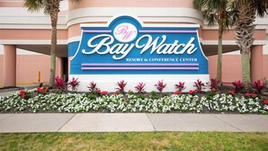 A sign for Bay Watch Resort & Conference Center with a clear view of the building's exterior and a flower bed in front. - Cozy 2-bedroom condo on the 10th Floor, located in fantastic North Myrtle Beach (North Myrtle Beach)