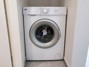 A compact, white front-loading washing machine with a control panel on the top. - Comfortable 1BR Apartment 5 min to Ladadika (Thessaloniki)