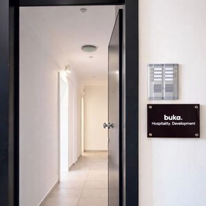 A hallway with a door leading to a room, a wall-mounted sign reading 'buka. Hospitality. Development', and a ventilation unit. - Comfortable 1BR Apartment 5 min to Ladadika (Thessaloniki)