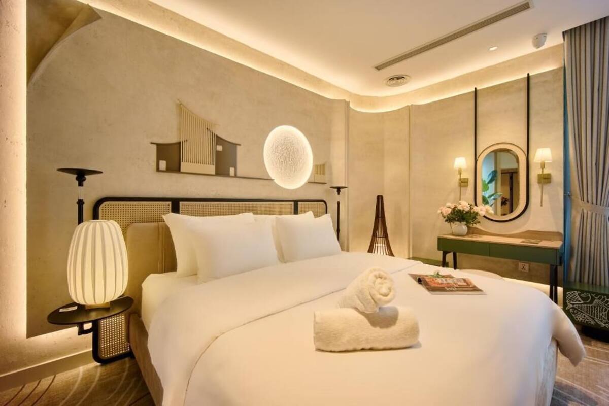 Una habitación de hotel con cama, mesita de noche, lámpara, espejo y una lámpara de pared.