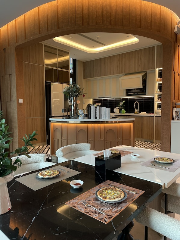 Una cocina moderna con paneles de madera, una zona de comedor con mesa de mármol negro y un sofá blanco.