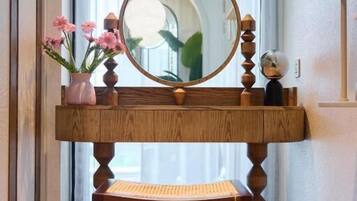 A wooden vanity with a mirror, a small stool, and a vase with pink flowers.