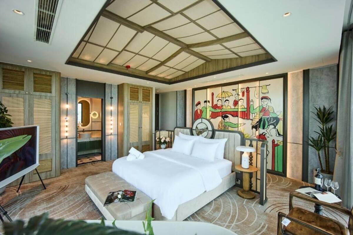 Una habitación de hotel moderna con una cama grande, televisión, escritorio y baño visible a través de una puerta de cristal.