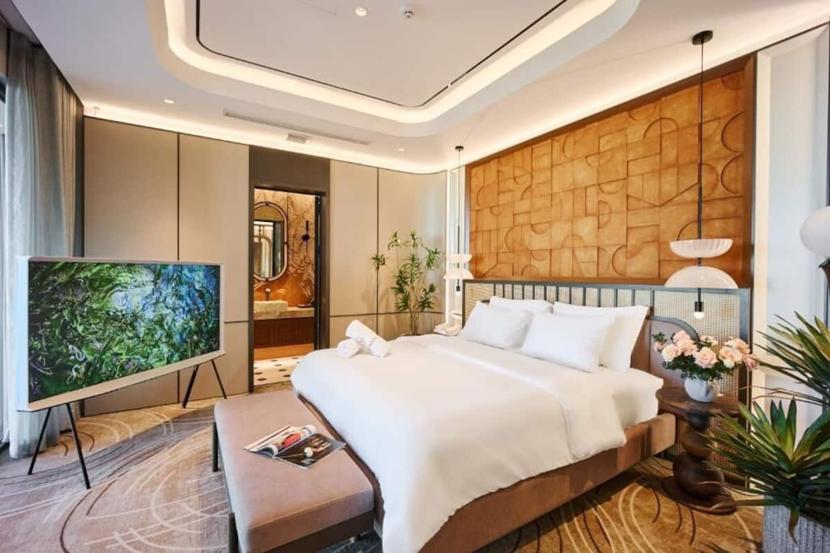 Una habitación de hotel moderna con una cama grande, un televisor de pantalla plana, una zona de estar y un muro decorativo.