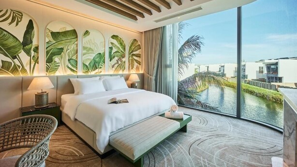 Una habitación de hotel moderna con una cama grande, vistas a una masa de agua y decoración mural con motivos tropicales.