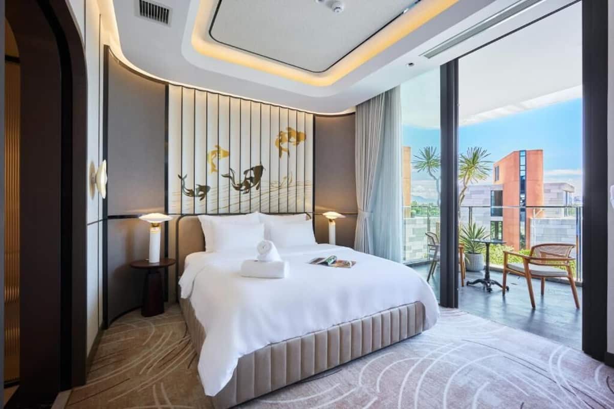 Habitación de hotel moderna con una cama grande, vistas de la ciudad y un balcón con mobiliario exterior.