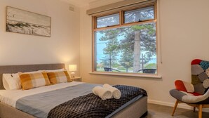 A bedroom with a bed, a window with a view of trees, a chair, and a painting on the wall.