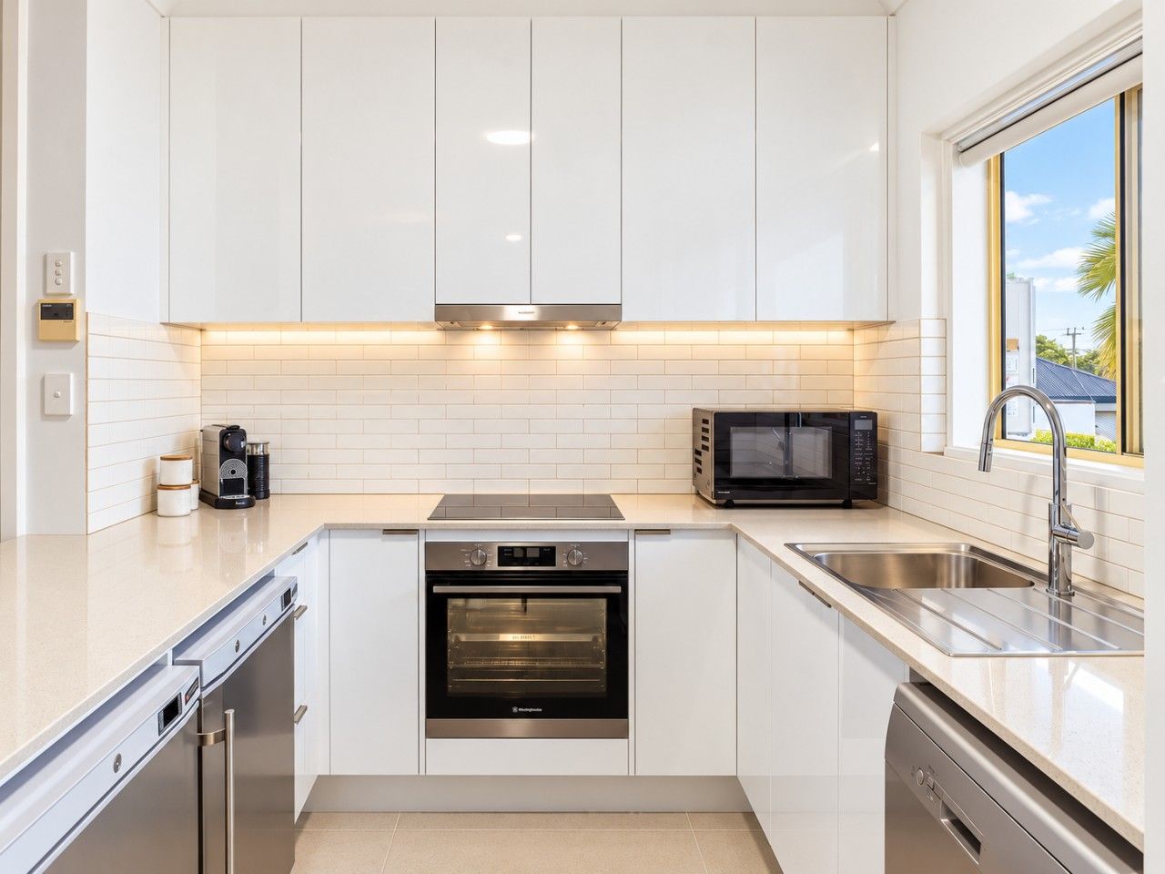 A modern kitchen with white cabinets, a built-in oven, a microwave, and a stainless steel sink.