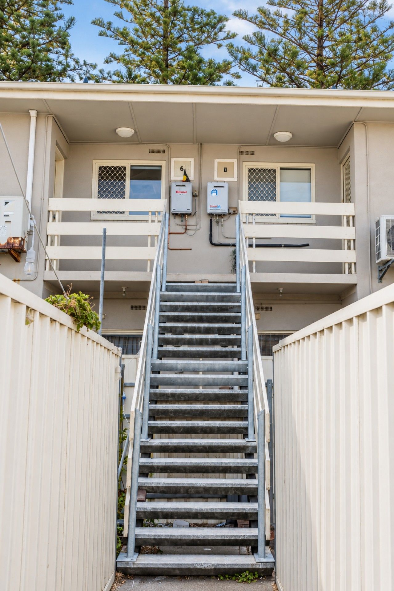 A set of metal stairs leading to a building with numbered windows and outdoor electrical boxes.