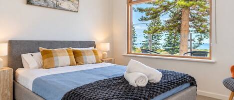 A bedroom with a bed, a window with a view of trees and the sky, and a painting on the wall.