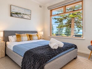 Un dormitorio con cama, ventana con vistas a árboles y cielo, y un cuadro en la pared.