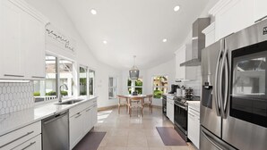 A modern kitchen with stainless steel appliances, white cabinetry, and a central island with seating. - Upscale Canal Home w/ Heated Pool & Spa (Marco Island)