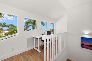 A room with a white desk, two windows with views of palm trees, a white railing, and a painting on the wall. - Upscale Canal Home w/ Heated Pool & Spa (Marco Island)