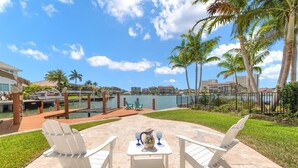 A patio with white chairs and a table, overlooking a marina with boats and a body of water. - Upscale Canal Home w/ Heated Pool & Spa (Marco Island)