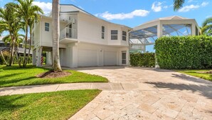 A modern two-story house with a covered garage, a well-maintained lawn, and a paved driveway. - Upscale Canal Home w/ Heated Pool & Spa (Marco Island)