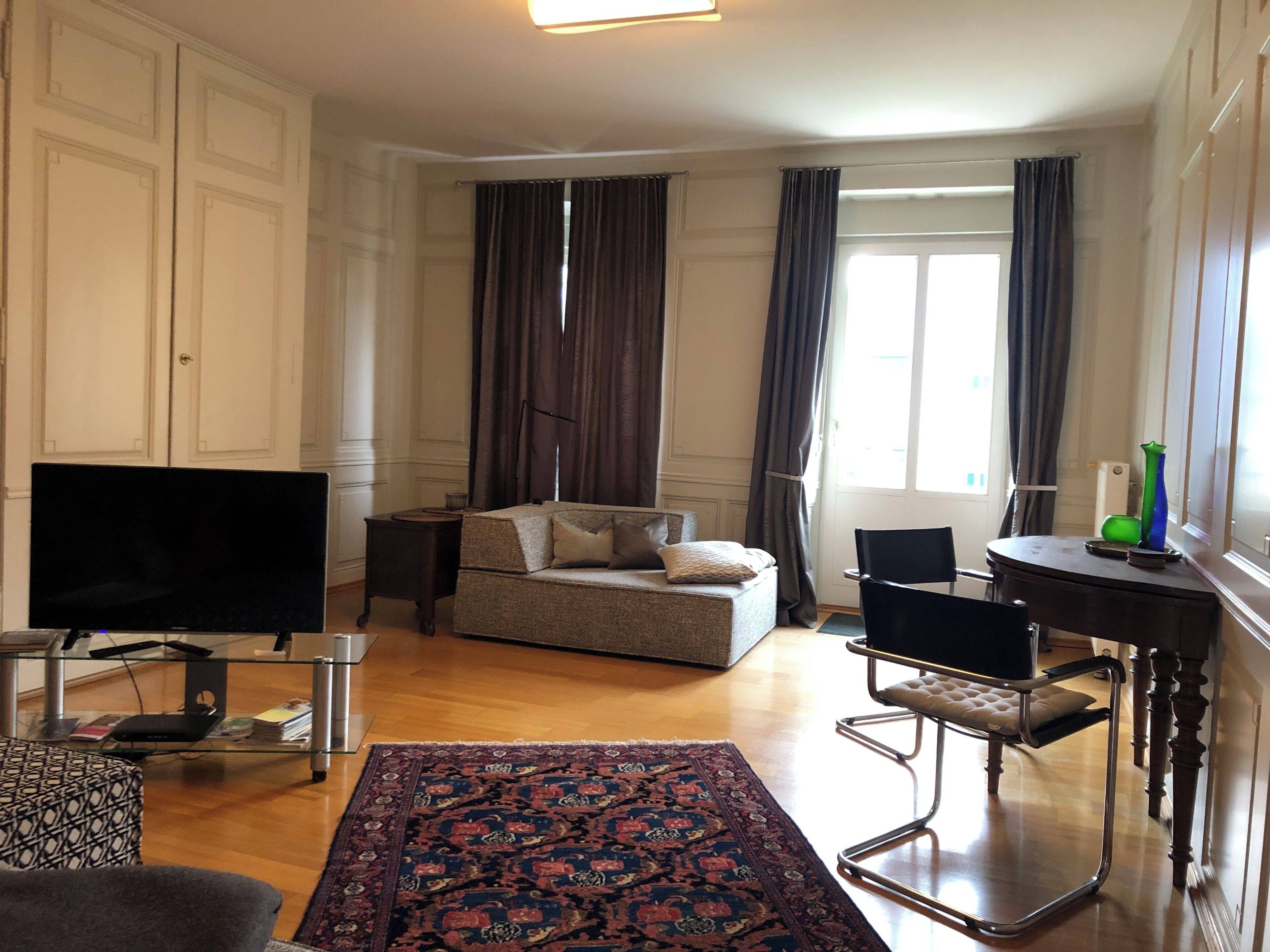 A living room with a sofa, a glass coffee table, a TV, a patterned rug, and a side table.