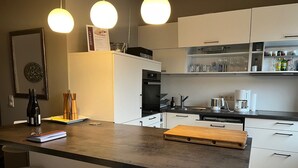 Moderni keittiö, jossa on keskeinen saareke, valkoiset kaapit ja riippuvalaisimet.
