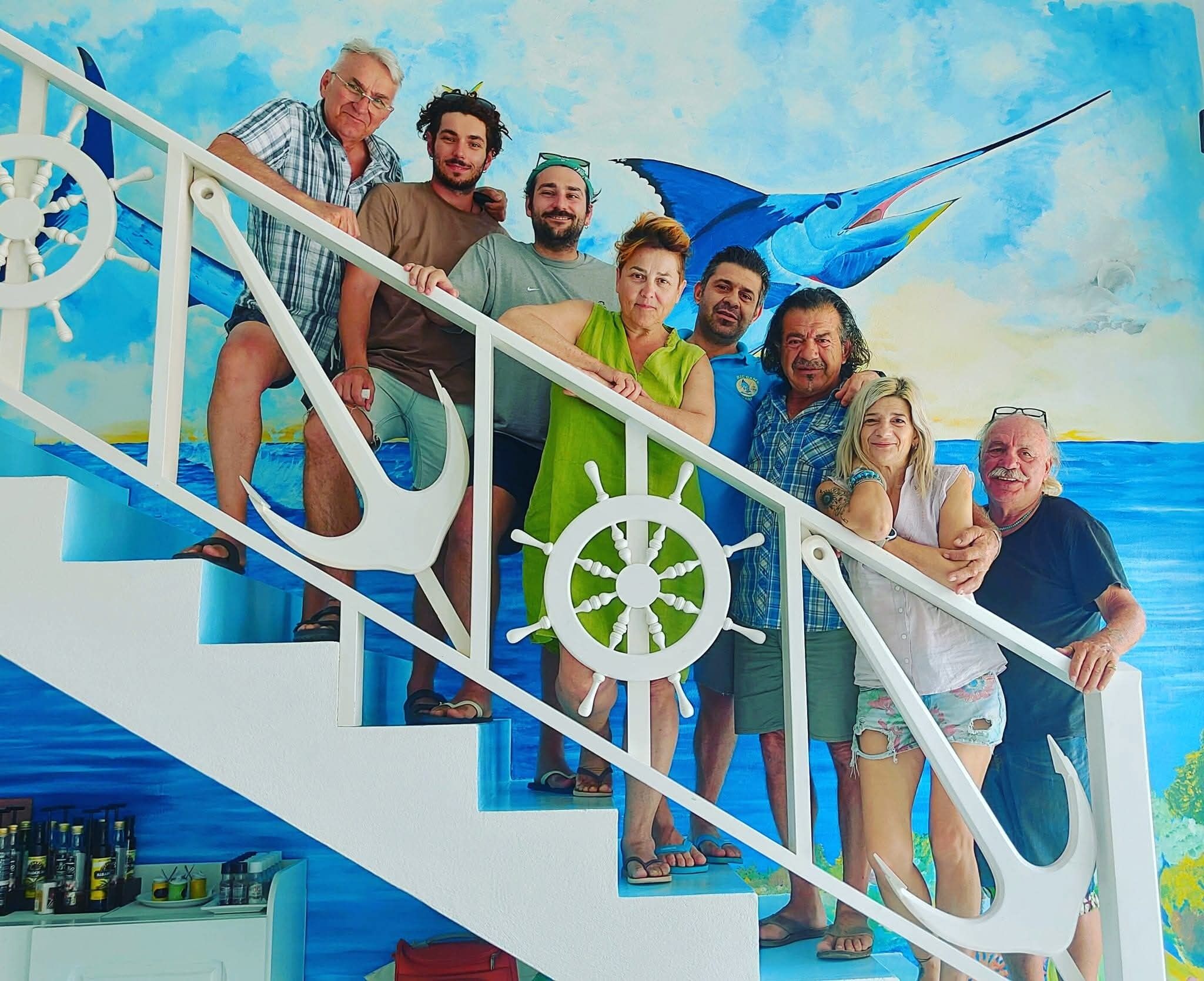 A group of people on a staircase with nautical-themed decor, including ship wheels and a sail.