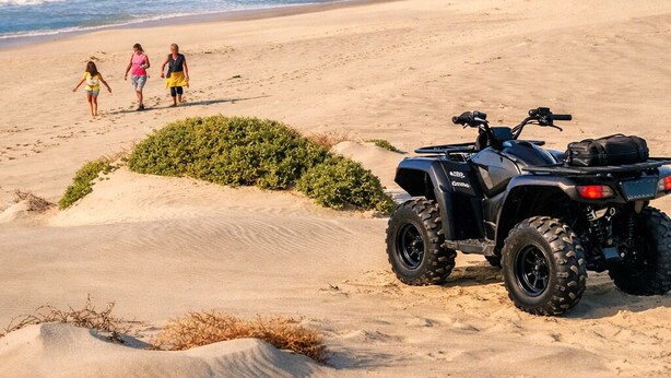 Una playa con dunas de arena, un buggy de dunas y tres personas caminando.