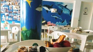 Una mesa de comedor con varios platos, una pared con un mural de tiburón y una habitación con vista al mar.