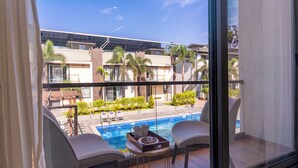 A balcony with two chairs, a small table, and a view of a swimming pool and buildings. - Alaya Stays Rosalia 3BHK Villa with Pool (Lonavala)
