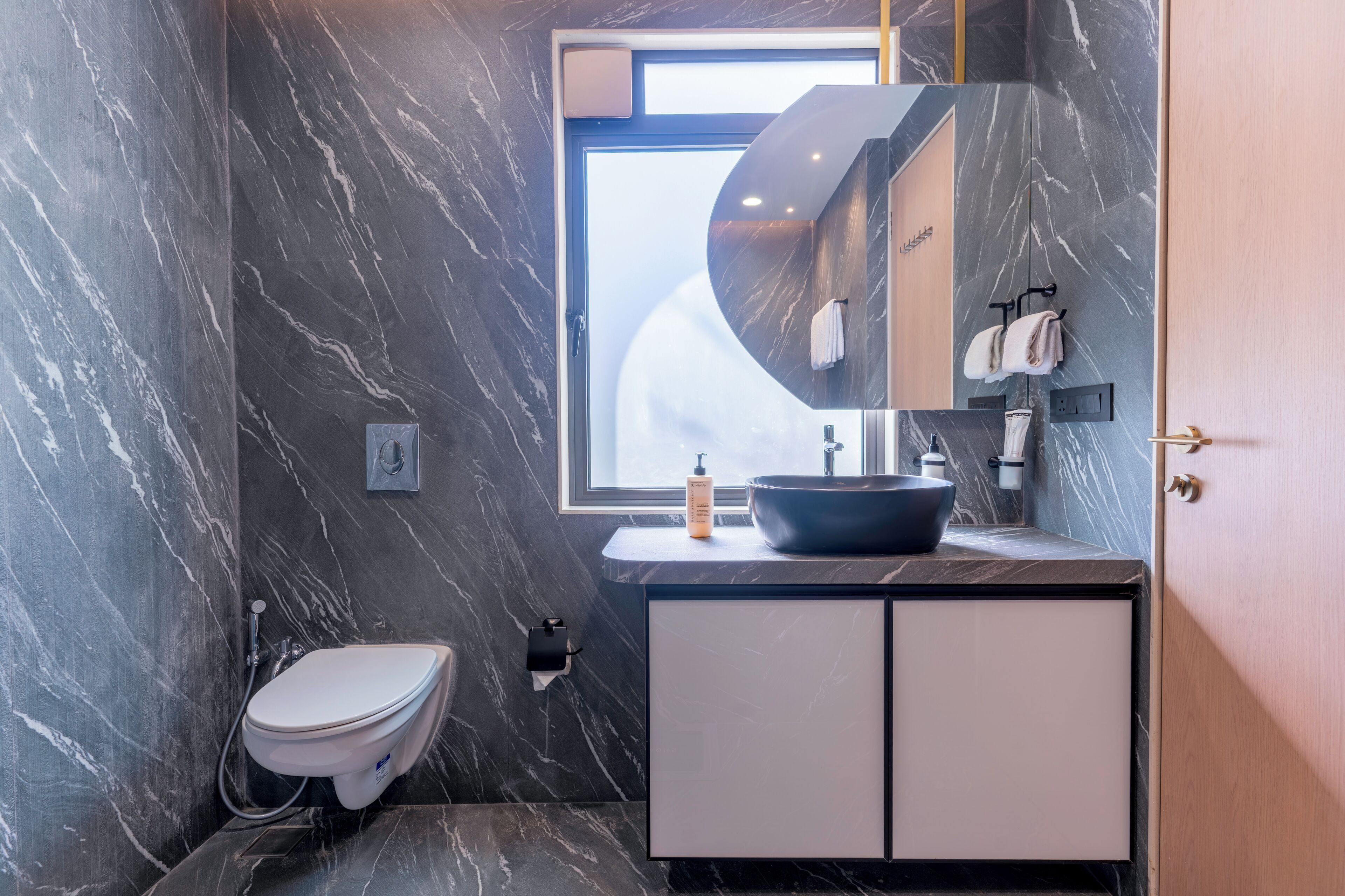Een moderne badkamer met een marmeren wand, een ingebouwd wastafelmeubel, een toilet en een raam.