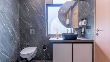 Een moderne badkamer met een marmeren wand, een ingebouwd wastafelmeubel, een toilet en een raam.