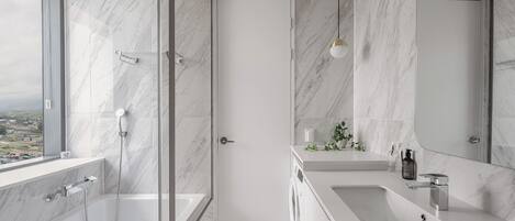 A modern bathroom with a glass-enclosed shower, a large mirror, and a view of the city.
