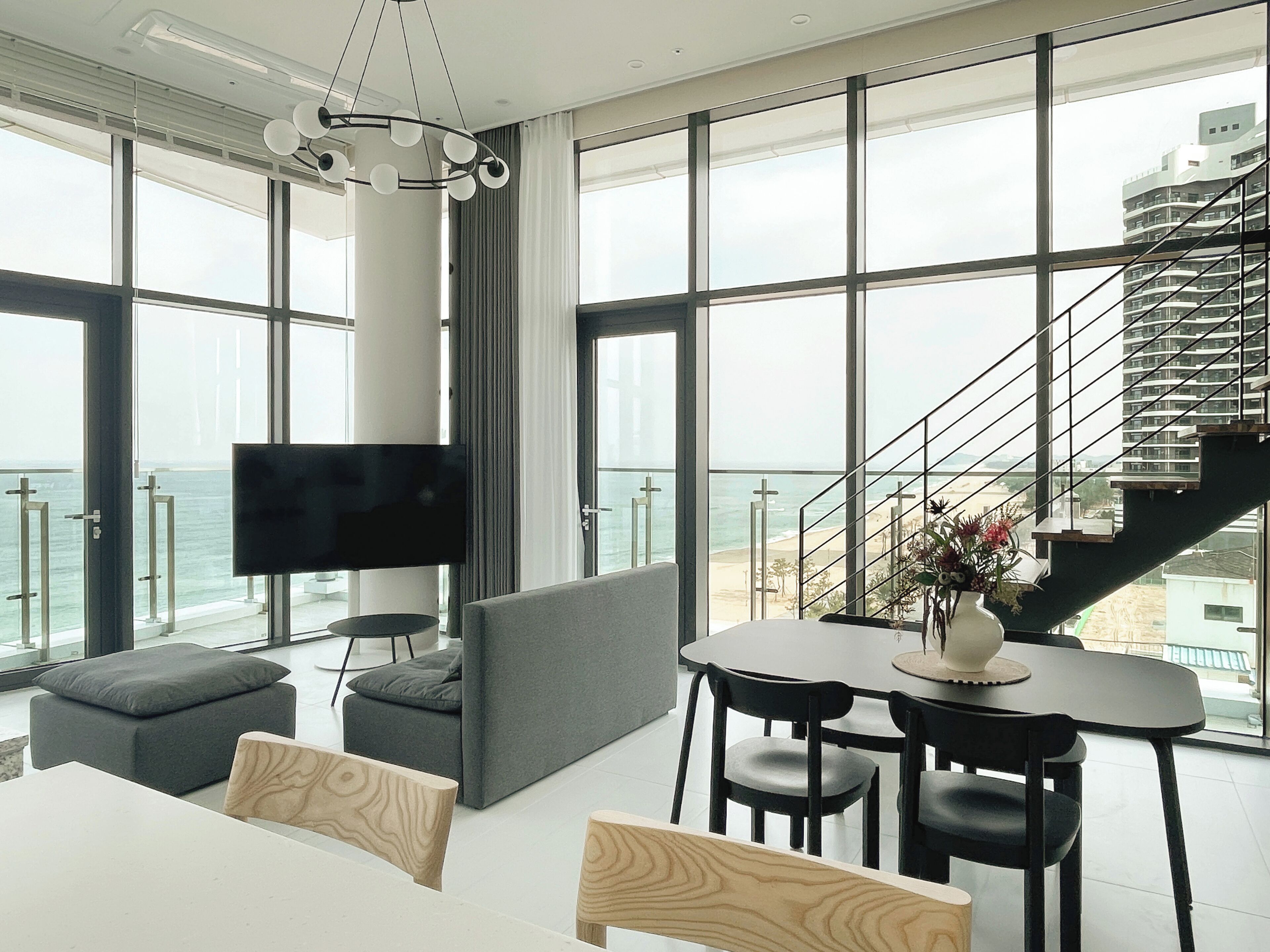 Een moderne woonkamer met een groot raam, een flatscreen televisie, een bank, een eettafel en een trap.