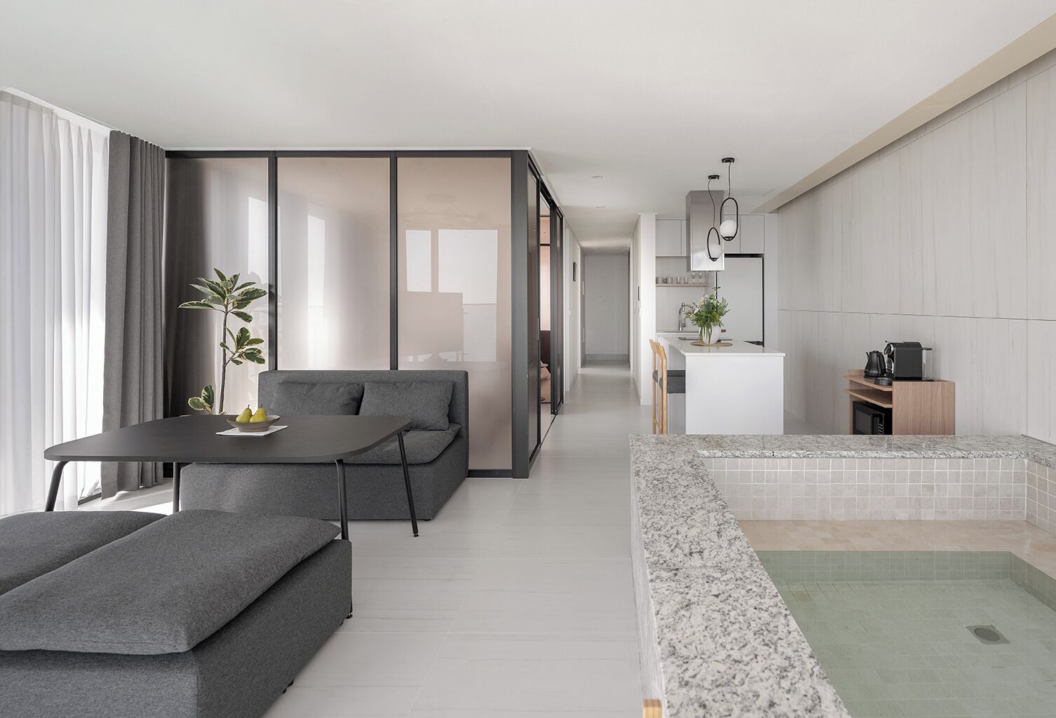 A modern living space with a sofa, a dining table, a kitchen area, and a small pool.