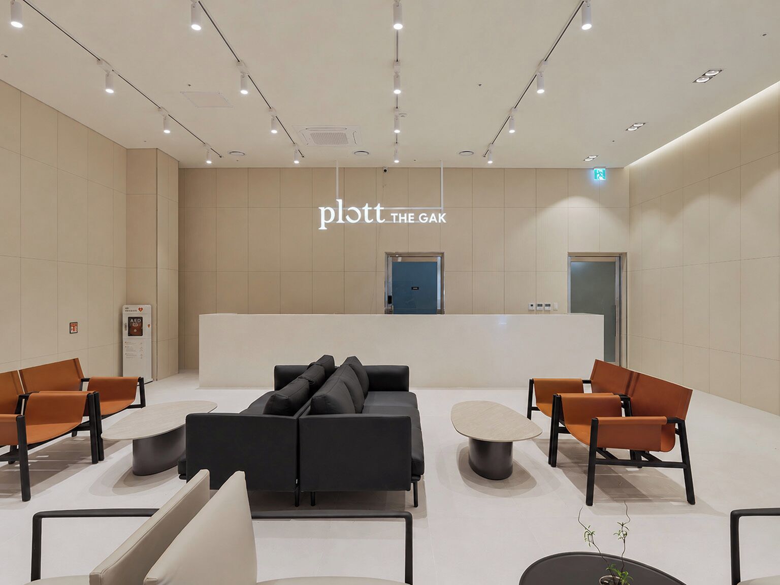 A modern reception area with a black sofa, orange chairs, a small table, and a sign reading 'plott THE GAK'.